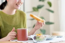 コーヒーカップを片手にトーストを食べる女性